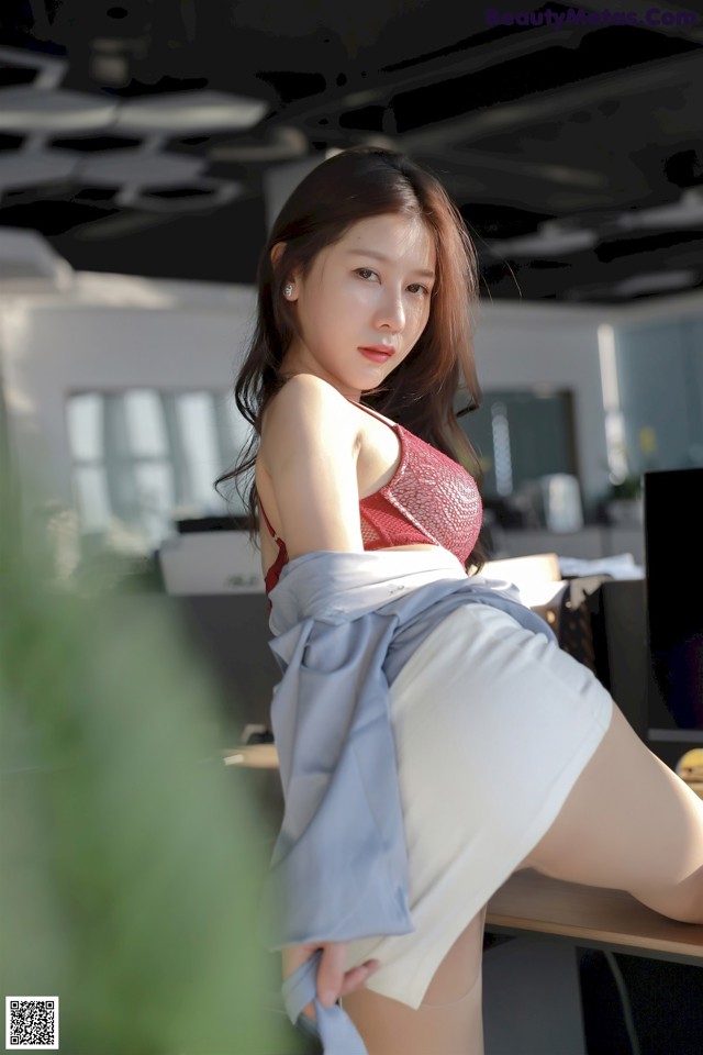 A woman in a red top and white skirt sitting at a desk.