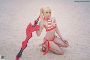 A woman in a bikini sitting on the beach holding a sword.