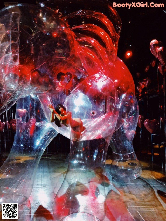 A woman in a red dress is sitting inside of a glass sculpture.