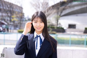 A woman in a school uniform leaning against a wall.