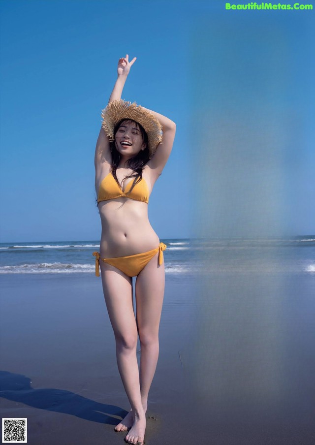 A woman in a yellow bikini standing on a beach.