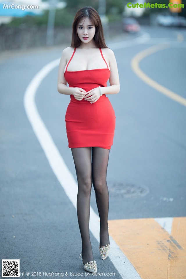 A woman in a red dress is standing on the street.