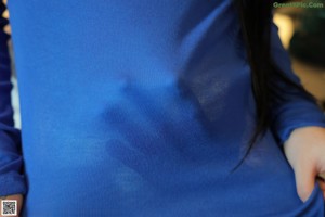 A woman sitting on a couch in a blue top and white skirt.