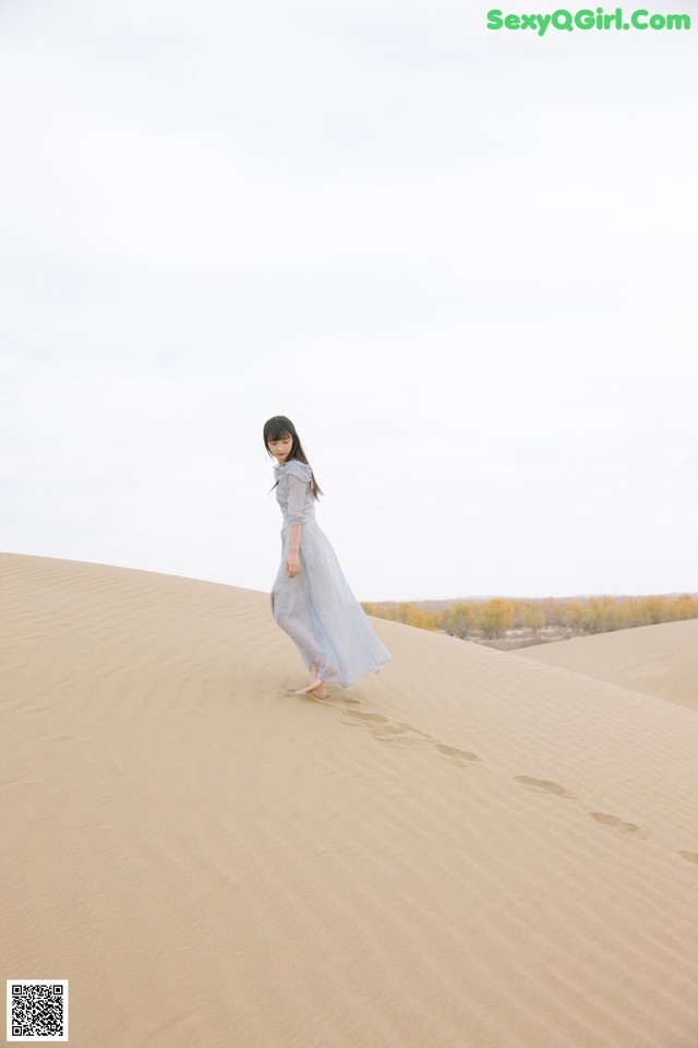 A woman in a blue dress walking on a sand dune.