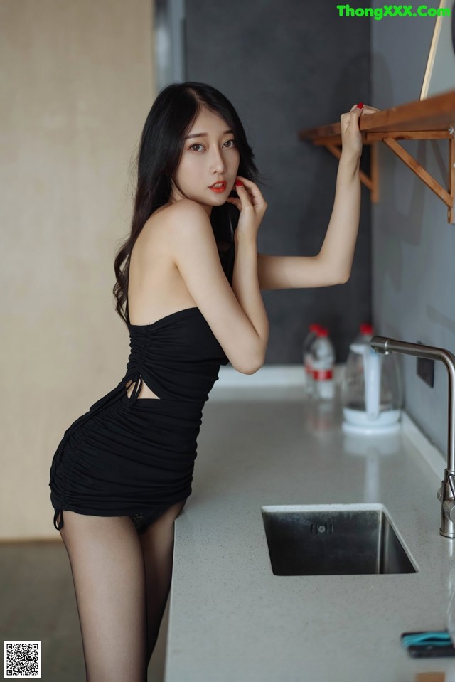 A woman in a black dress standing in a kitchen.