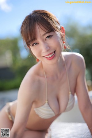 A woman in a bikini sitting by a swimming pool.
