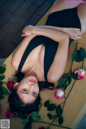 A woman laying on a bed next to a pink rose.