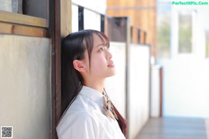 A young woman sitting on a white chair wearing a school uniform.