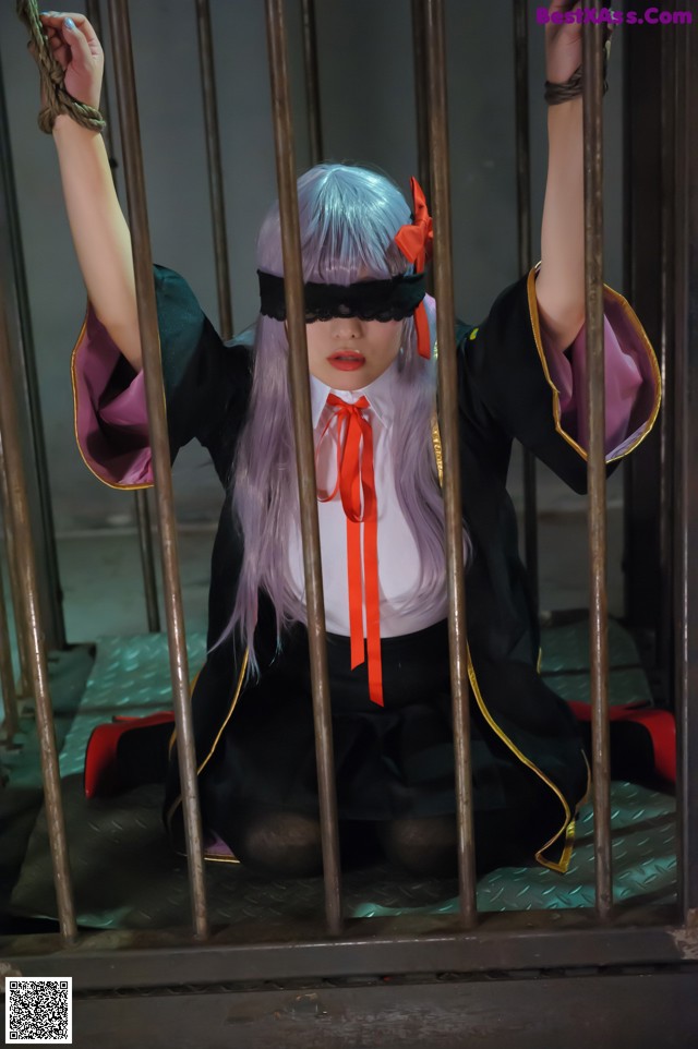 A woman in a black and purple outfit is tied up to a cage.