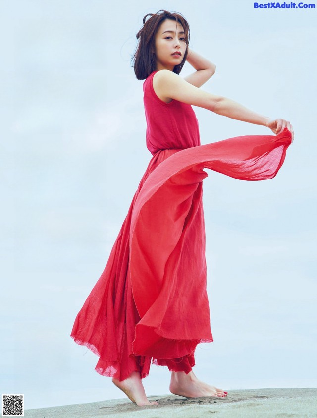 A woman in a red dress standing on a beach.