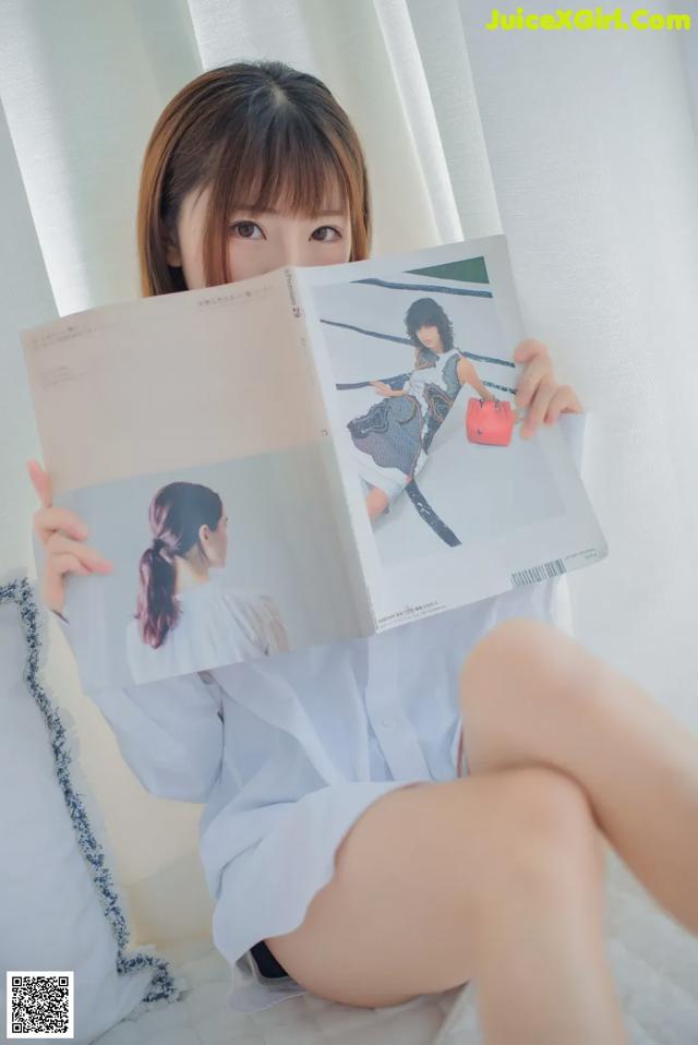 A woman sitting on a bed holding a magazine.