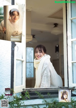 A woman in a white sweater leaning against a wall.