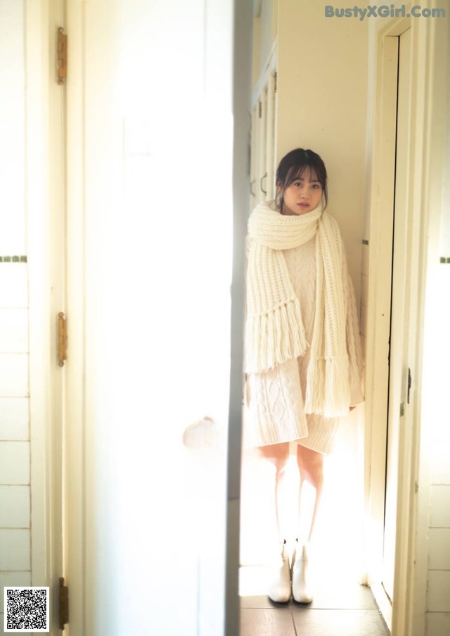 A woman standing in a doorway wearing a white sweater and scarf.