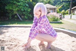 A woman in a purple and white dress kneeling on a sandy beach.