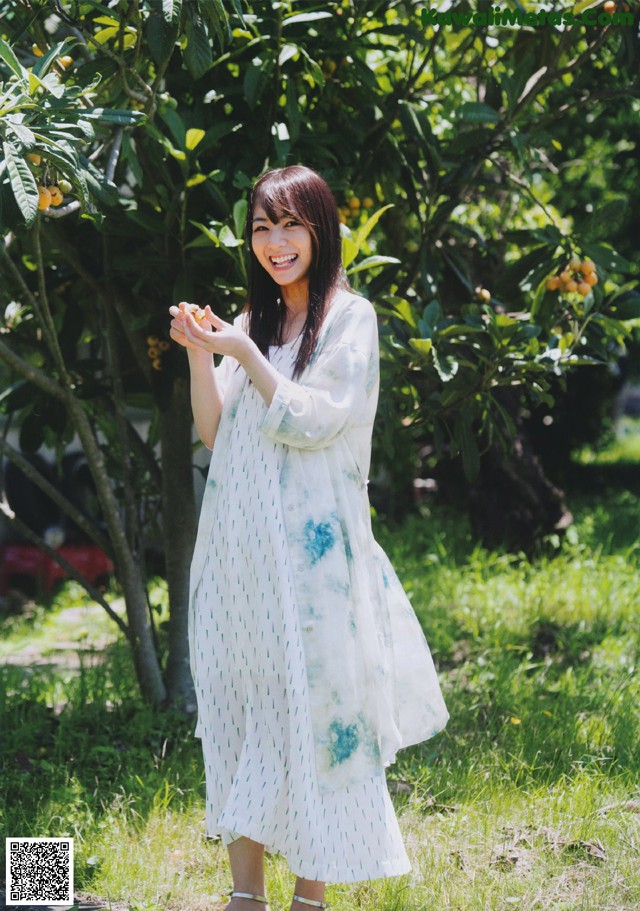 A woman standing in front of an orange tree holding an orange.