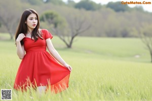 A woman in a red bodysuit sitting on a bed.