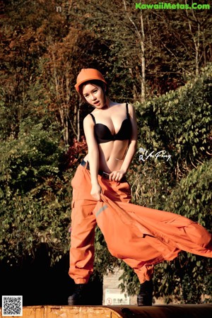 A woman in a black bra top and orange pants posing on a train track.