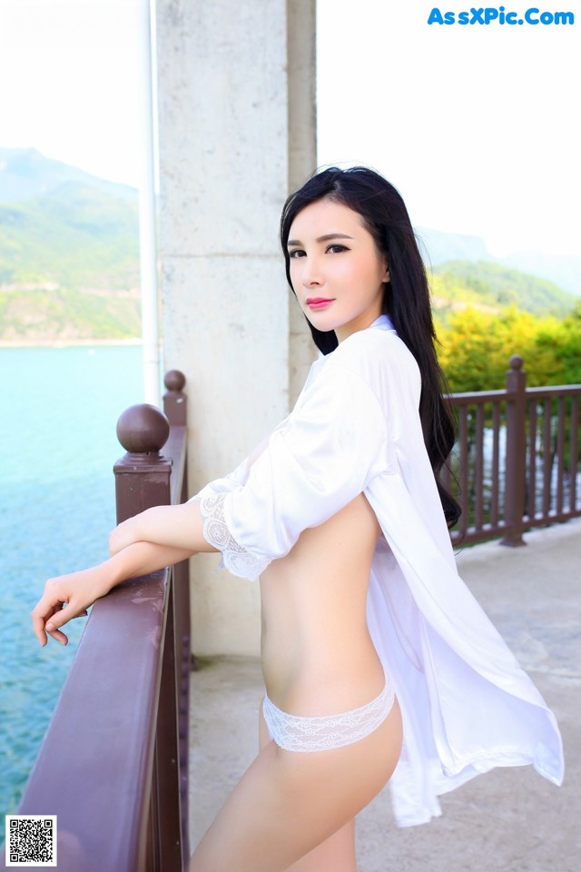 A woman in a white shirt and panties posing on a balcony.