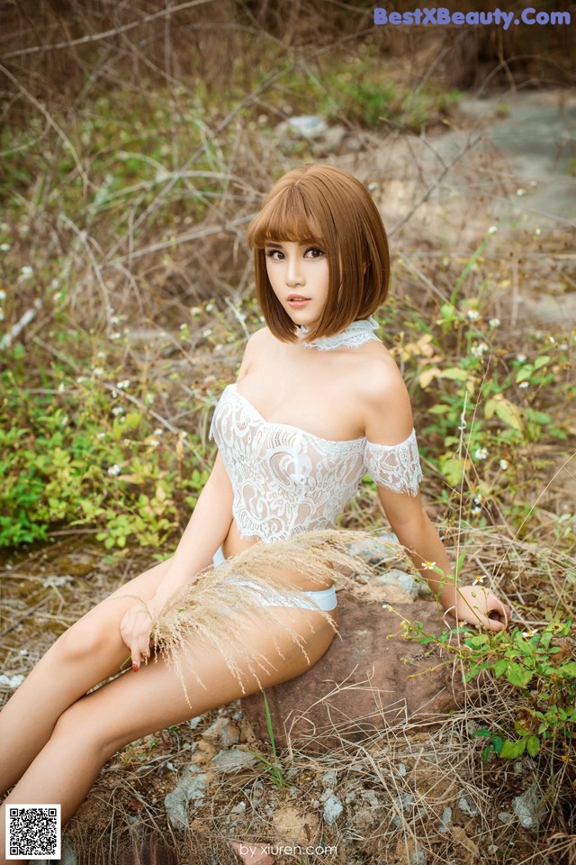 A woman in a white lingerie sitting on a rock.