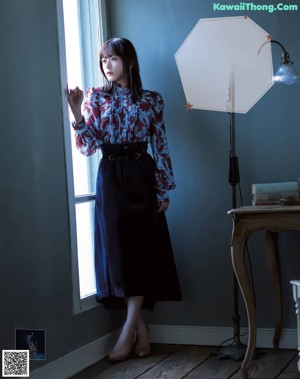 A woman in a red and blue floral shirt is looking out a window.