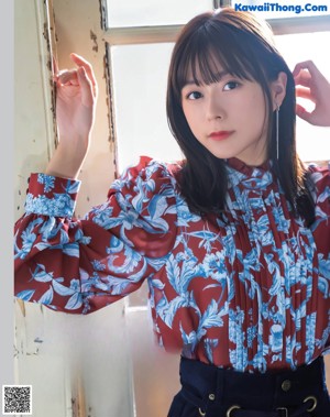 A woman in a red and blue blouse leaning against a window.