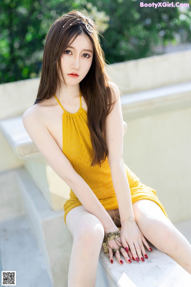 A woman in a yellow dress sitting on a ledge.