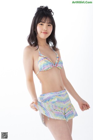A woman in a bikini top and shorts leaning against a wall.