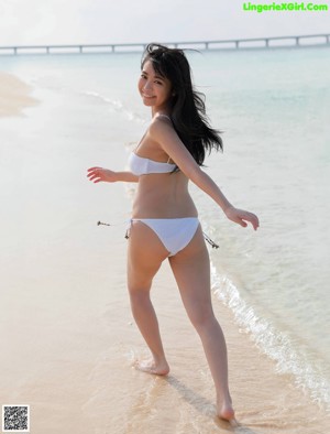 A woman in a white bikini standing in the water.