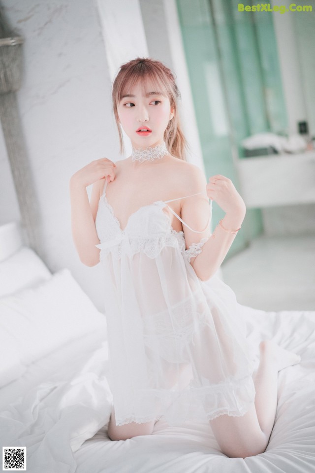 A woman in a white lingerie sitting on a bed.