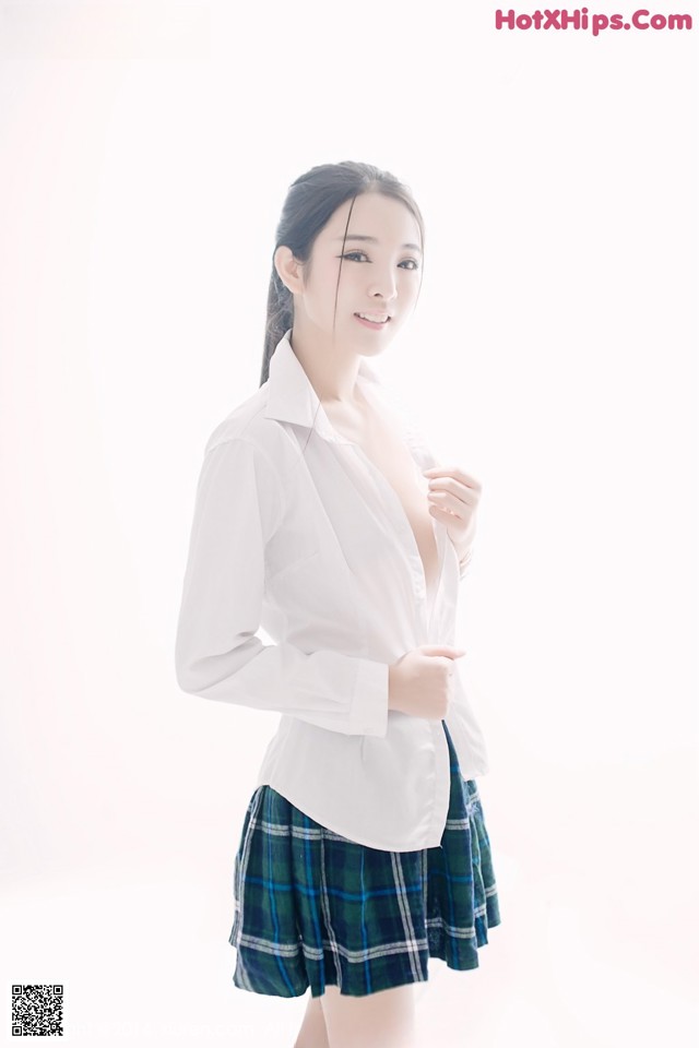 A woman in a white shirt and plaid skirt posing for a picture.