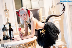 A woman dressed as a devil sitting at a table with a glass of wine.