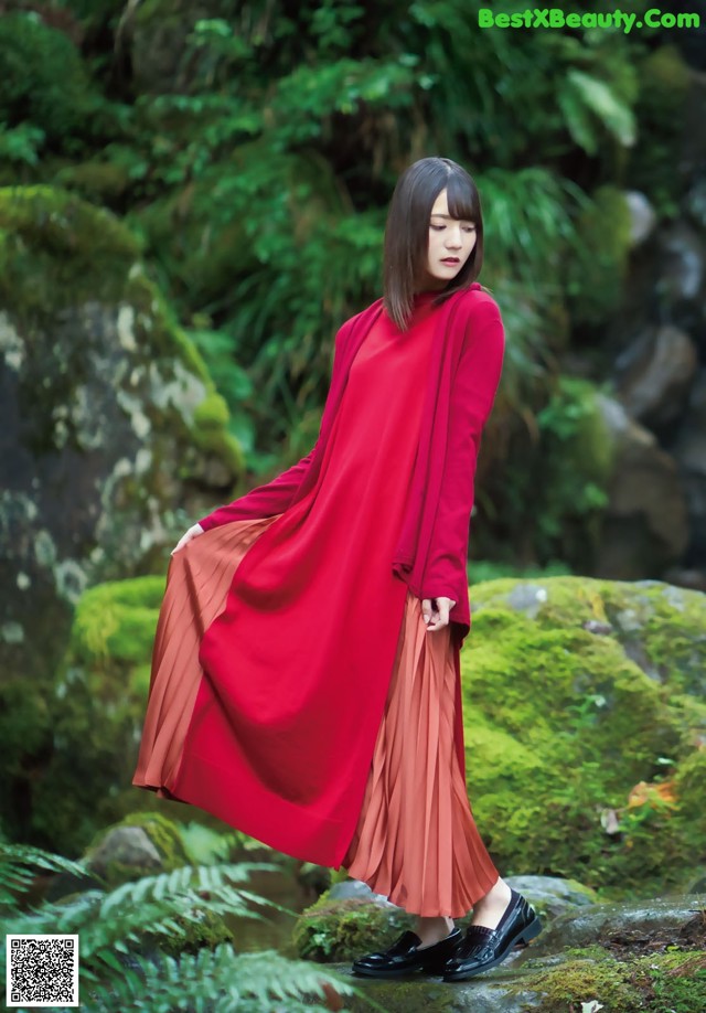 A woman in a red dress standing on a rock in a forest.