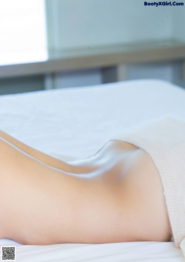 A woman laying on top of a bed covered in a white sheet.