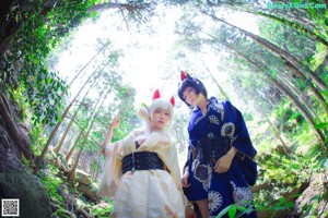 A couple of women sitting on top of a rock in the woods.