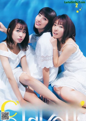 A group of three young women sitting on a blue surface.