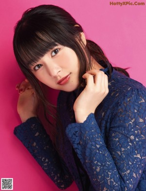 A woman in a blue lace top leaning against a pink wall.