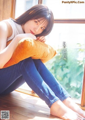 A woman sitting on a wooden bench in a white shirt and blue jeans.